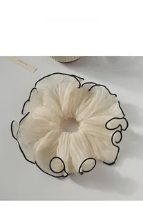 Detail of a large cream scrunchie with black contrast edges and pleated chiffon texture