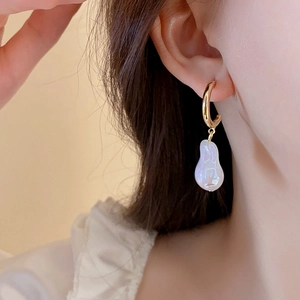 Close-up of elegant gold hoop earrings with large baroque pearl drops on a model