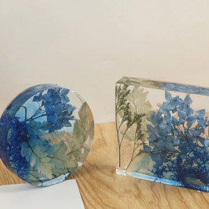 Detail of round and rectangular resin coasters with blue hydrangea and green leaves