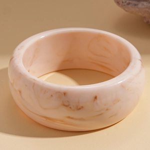 Detail of wide resin bangle featuring peach pink marble patterns and smooth texture