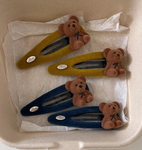 Detail of four flocked bear hair clips with Love metal studs in blue and yellow colors