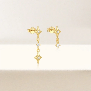 Detailed view of gold star dangle earrings with sparkling round zircon on beige surface