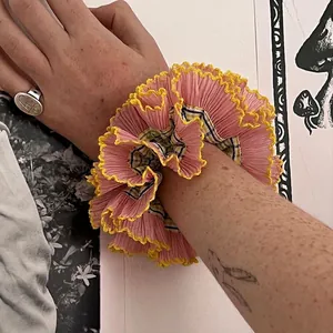 Pink oversized cotton scrunchie with yellow lace trim and plaid lining on a wrist