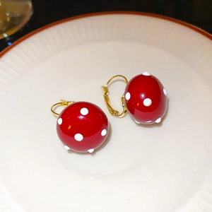 Close-up of red polka dot pearl earrings in a white ceramic dish with gold扣 accent