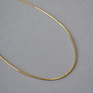 Collana choker minimalista in ottone dorato a molla su uno sfondo grigio materico