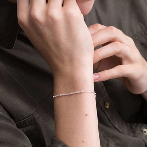 Close-up of minimalist layered silver chain bracelet worn on wrist with tiny beads