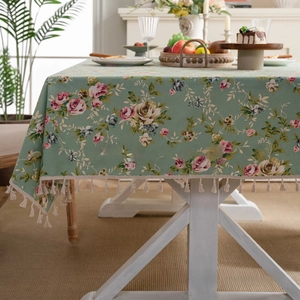 Detail of green floral linen tablecloth featuring pink roses and decorative cream tassels