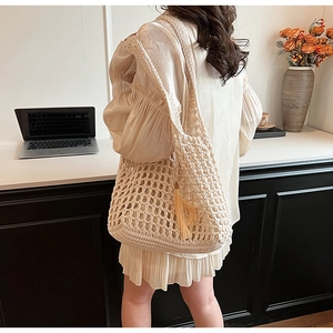 Detail of a cream crochet tote bag with fringe tassel carried by a model in a minimal setting