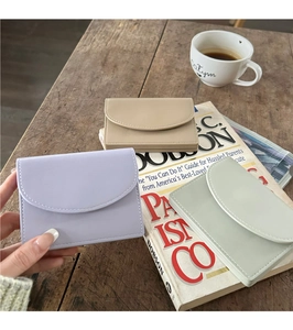 Three minimalist PU leather wallets in purple, beige and green on a wooden table