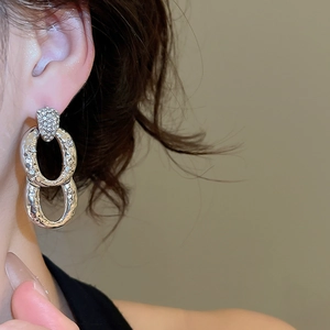 Close-up of silver textured double-loop earrings with zircons and hammered metal finish