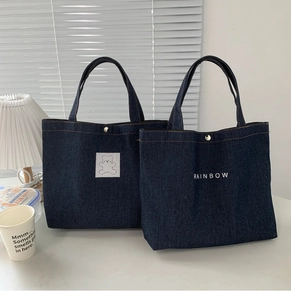 Detail of dark blue denim tote bags with bear patch, rainbow embroidery and magnetic closure