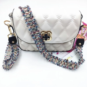 White quilted crossbody bag with colorful woven strap and golden floral clasp