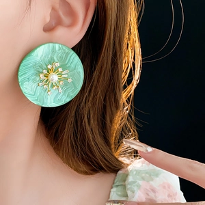 Nahaufnahme eines grünen Harzohrrings mit goldenem Blumendesign und Perle am Model