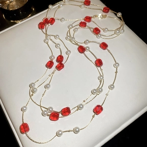 Detail of multi-layered gold necklace featuring red crystal beads and white pearls