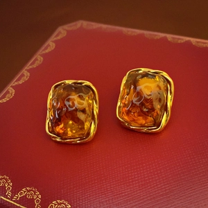 Close-up of geometric amber resin earrings with gold twisted rope borders on a red box