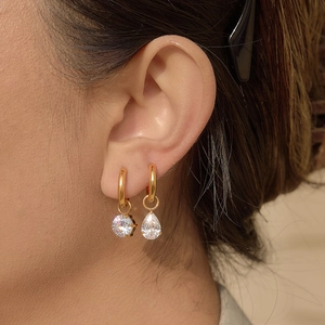 Elegant gold hoop earrings set with round and pear-cut zircon pendants on female model