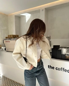 Detailed view of a white faux leather cropped jacket with flap pockets and ribbed cuffs
