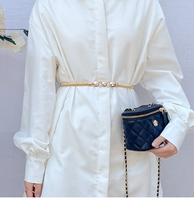 Detail of gold metal elastic belt with rhinestone buckle on white dress and black bag