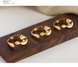 Detail of three gold liquid wave rings with a high-polished finish on a wooden stand