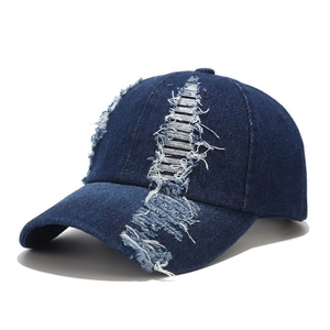Macro detail of distressed denim texture and frayed holes on a dark blue baseball cap