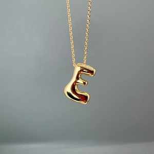 Close-up of golden letter E pendant on a fine O-chain with polished metallic finish