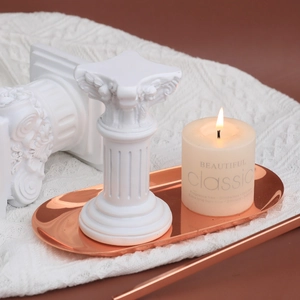 White unscented pillar candle on a Roman column stand with rose gold tray and blanket
