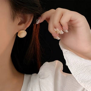 Close-up of vintage round opal stud earring with gold woven metal frame on model's ear