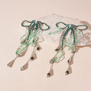 Detailed shot of green rhinestone bow earrings with silver tassels on a white stone