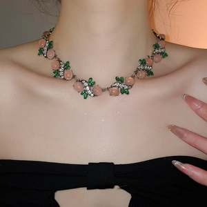 Close-up of vintage resin necklace featuring pink gemstones and green leaf-shaped crystals