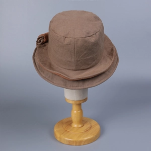 Detail of a dark brown linen bucket hat with a fabric flower ornament on a wooden stand
