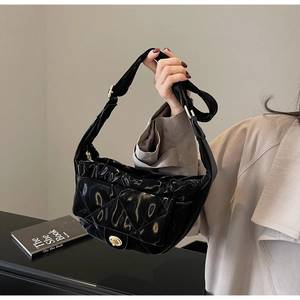 Detail of black quilted patent leather bag with a gold turn-lock and adjustable strap