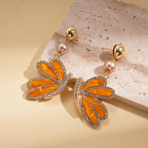 Vue macro de boucles d'oreilles papillon en acétate orange avec dorure et strass brillants