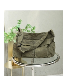 Detail of olive green canvas messenger bag showing texture and stitching on a glass table