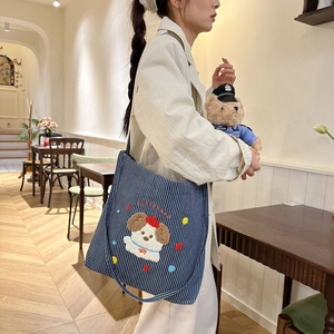 Detail of blue striped canvas tote bag featuring cute cartoon puppy embroidery on shoulder