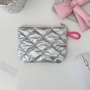 Detail view of silver quilted makeup bag with pink knotted zipper pull on a white desk