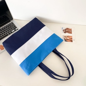 Detail showing the heavy-duty woven canvas texture and tricolor stitching of the tote bag