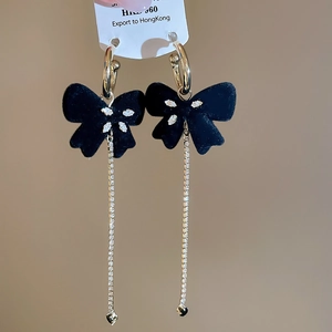 Detail of gold hoop earrings featuring black flocked bows and long rhinestone tassels