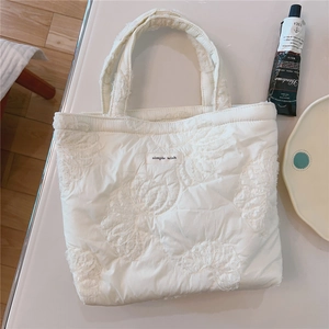 Detail of white quilted tote bag featuring floral embroidery and simple wish label