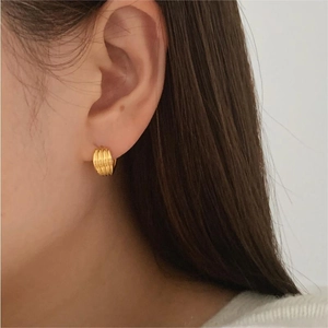 Close-up of a minimalist gold hoop earring with textured relief on model's ear