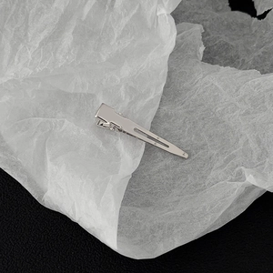 Macro shot of long silver metal duckbill hair clip with polished finish on white paper