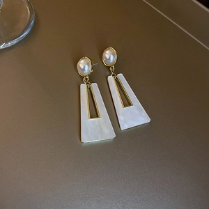 Detailed close-up of geometric gold earrings with white marble resin drop pendants
