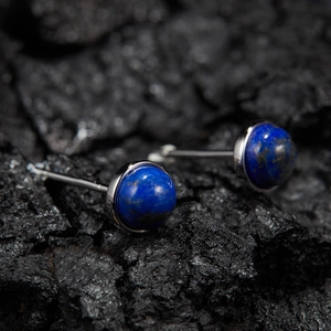 Macro shot of silver stud earrings with round blue lapis lazuli on dark volcanic stone