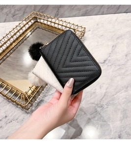 Detail of V-quilted faux leather wallet with matching plush ball charm on marble background