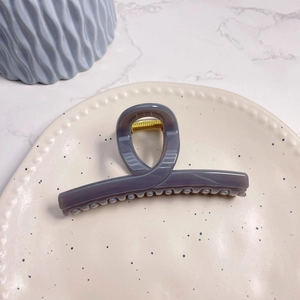 Detail of a large matte grey hair claw clip on a ceramic tray with a golden spring
