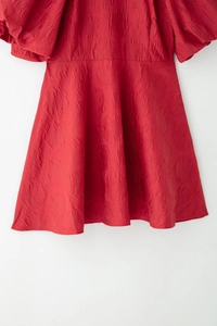Détail de la robe rouge à manches bouffantes montrant la texture plissée du tissu