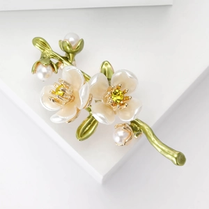 Macro detail of plum blossom brooch with white petals, green stems, and pearls on white stand