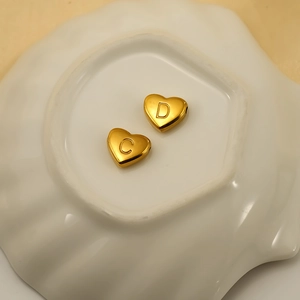 Golden heart-shaped titanium steel beads engraved with letters C and D on a ceramic tray