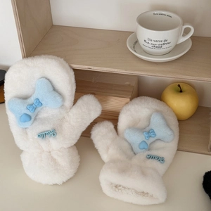 Close-up of white plush mittens with blue Hello lettering and soft bow on wooden shelf