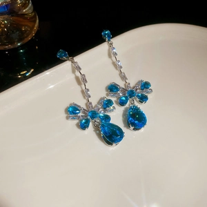Detailed close-up of blue bow zircon drop earrings on a white plate with soft lighting