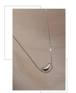 Macro shot of silver bean pendant with a high-polished mirror finish on a woven background